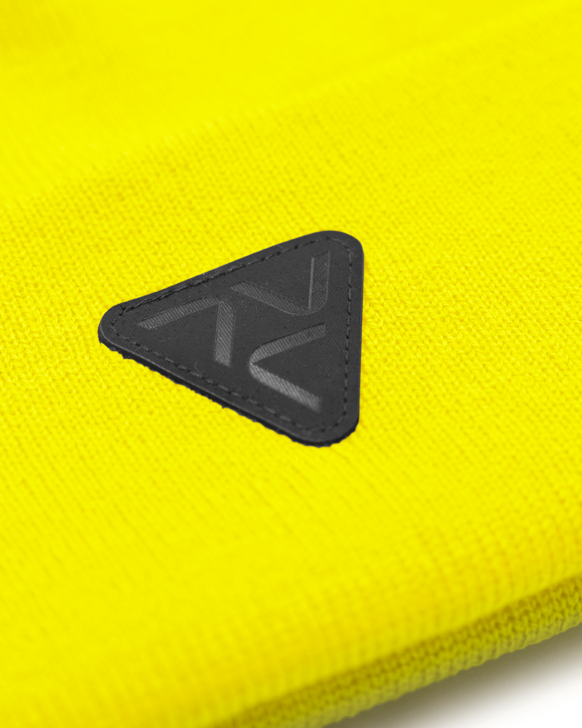 Close-up of Vohl Hi Vis Beanie in Safety Yellow showing black triangular logo patch and knit texture - SKU AC-BN-100-OS | color:Safety Yellow