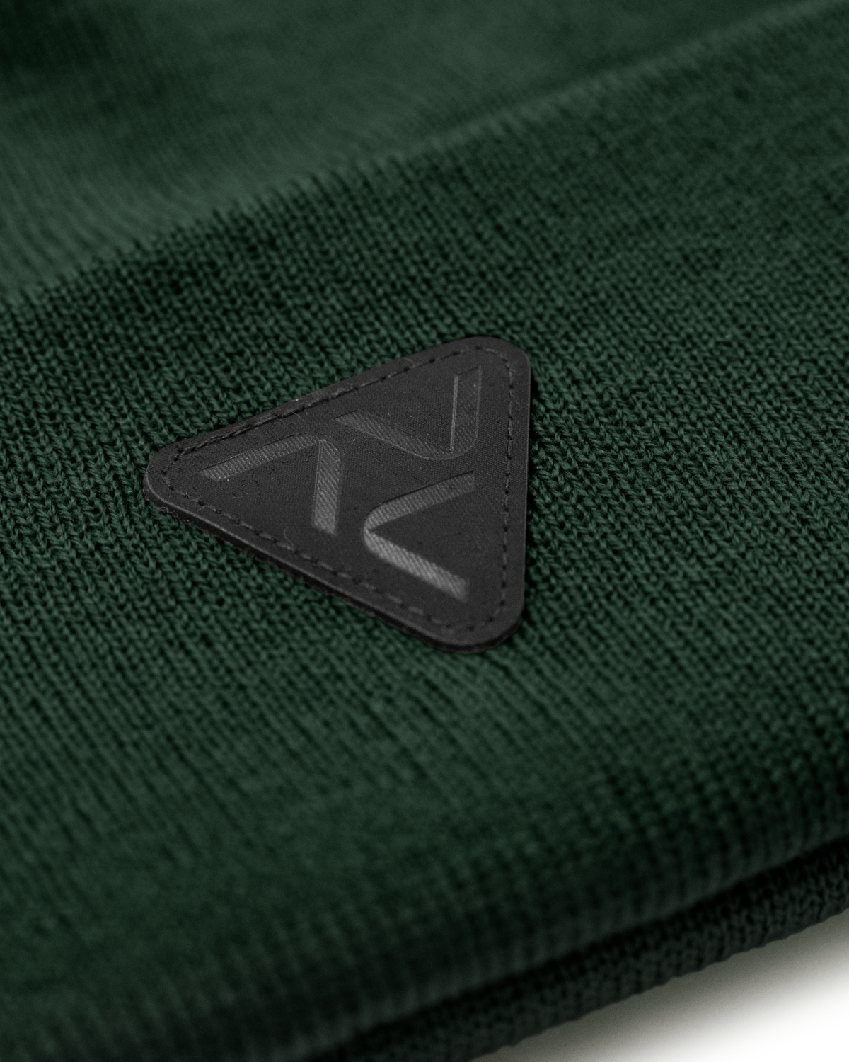 Close-up of Vohl Beanie in Deep Forest Green showing black triangular logo patch and knit texture - SKU AC-BN-400-OS | color:Deep Forest Green