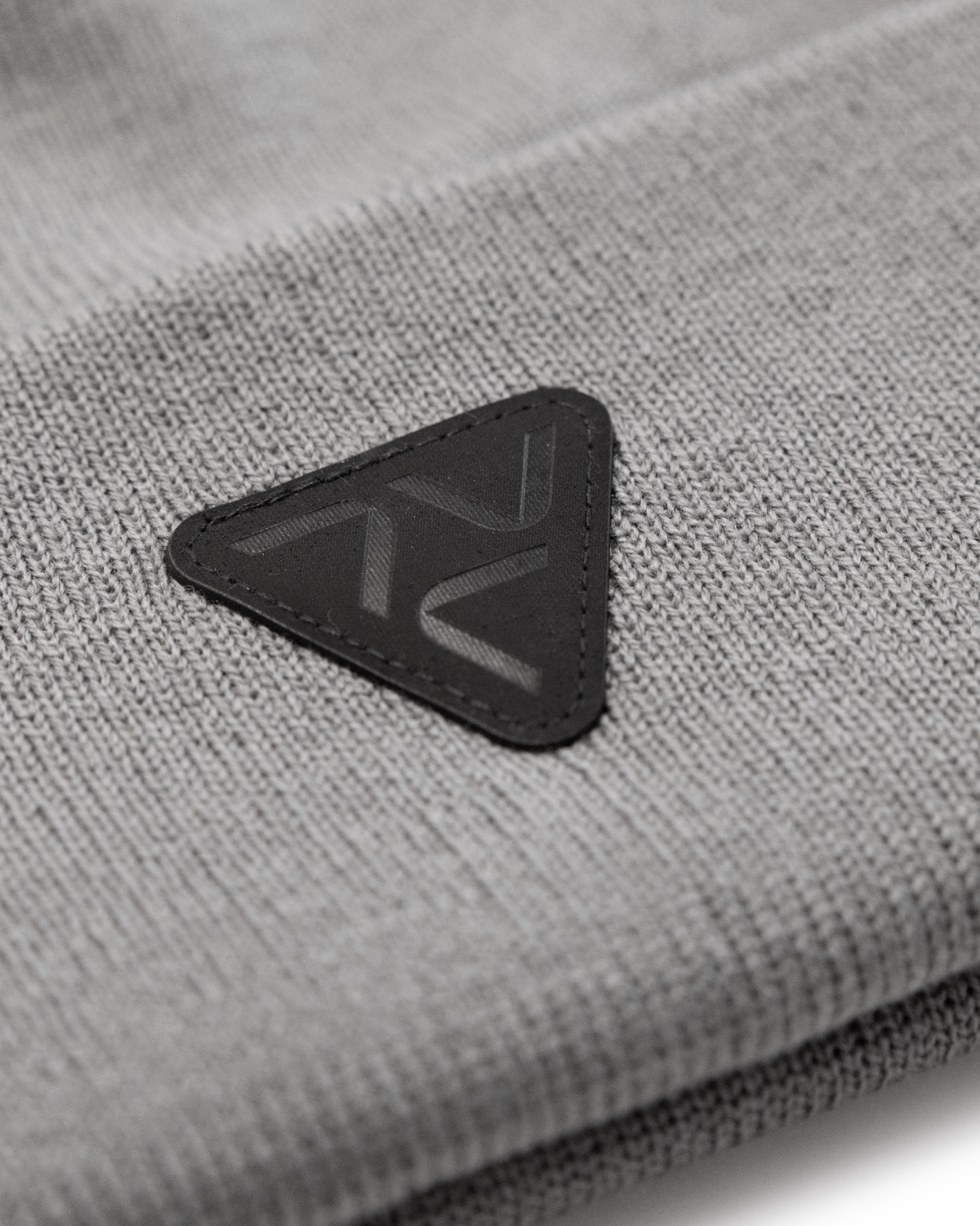 Close-up of Vohl Beanie in Pewter showing black triangular logo patch and knit texture - SKU AC-BN-700-OS | color:Pewter