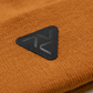 Close-up of Vohl Beanie in Tobacco showing black triangular logo patch and knit texture - SKU AC-BN-800-OS | color:Tobacco