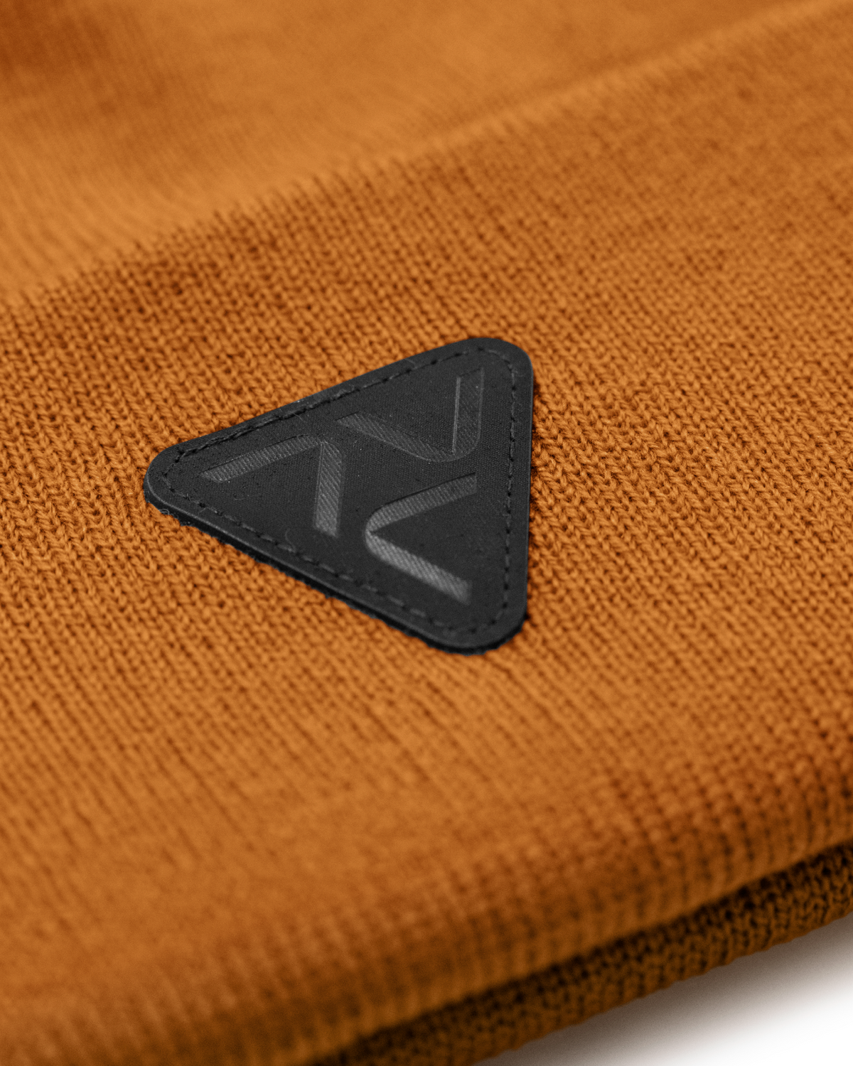 Close-up of Vohl Beanie in Tobacco showing black triangular logo patch and knit texture - SKU AC-BN-800-OS | color:Tobacco